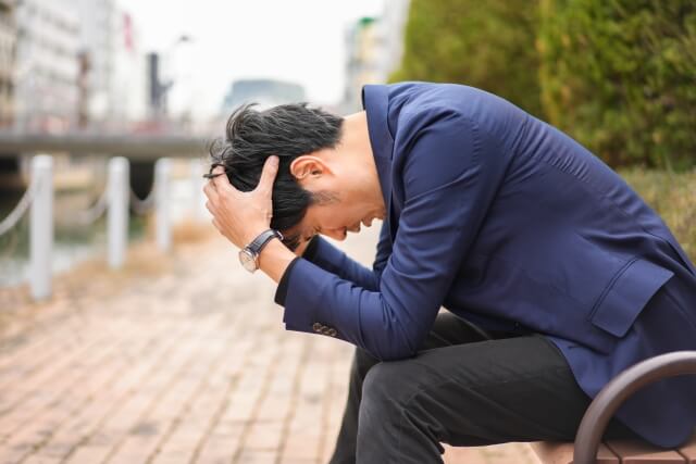 悩むビジネスマンが公園で考える